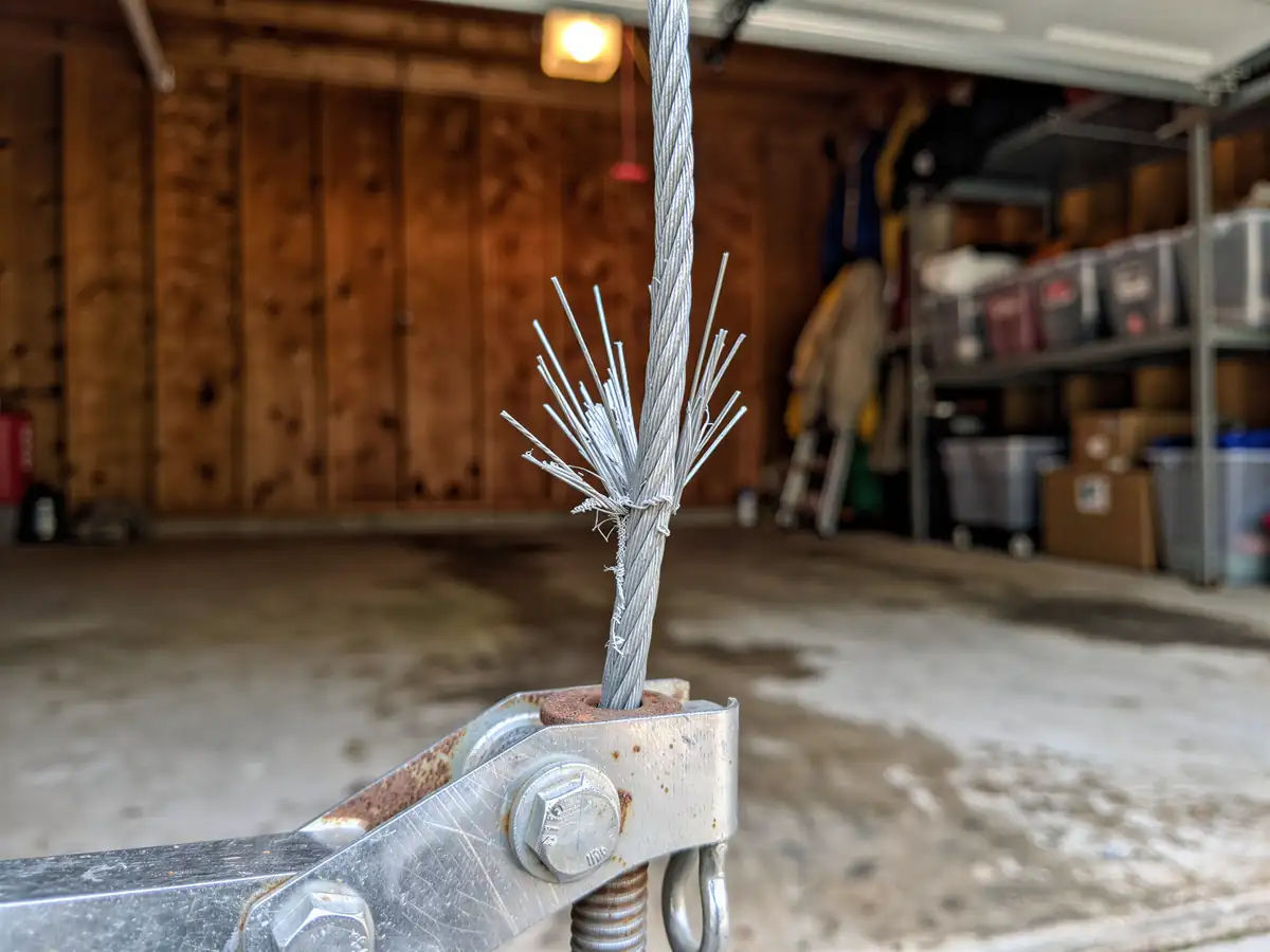 The frayed garage door cable is attached to a metal bracket in a garage.
